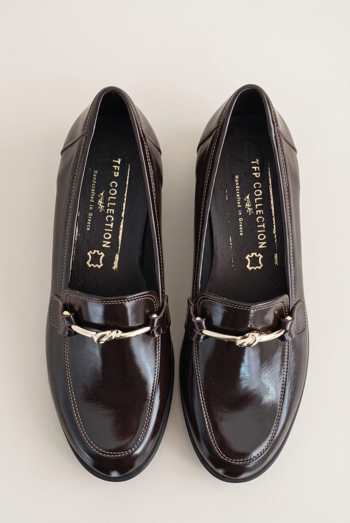 Top view of a pair of brown patent horsebit loafers with rounded toes and gold bit details on the vamp