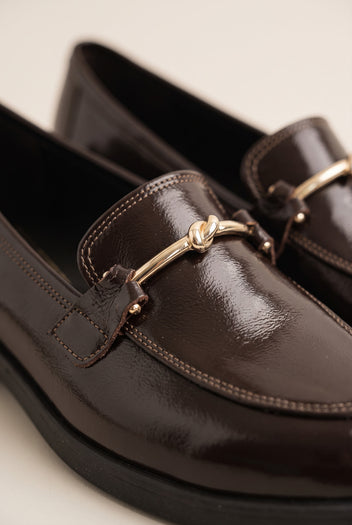 Close-up of brown glossy patent leather loafer vamp with a gold horsebit and contrast topstitching