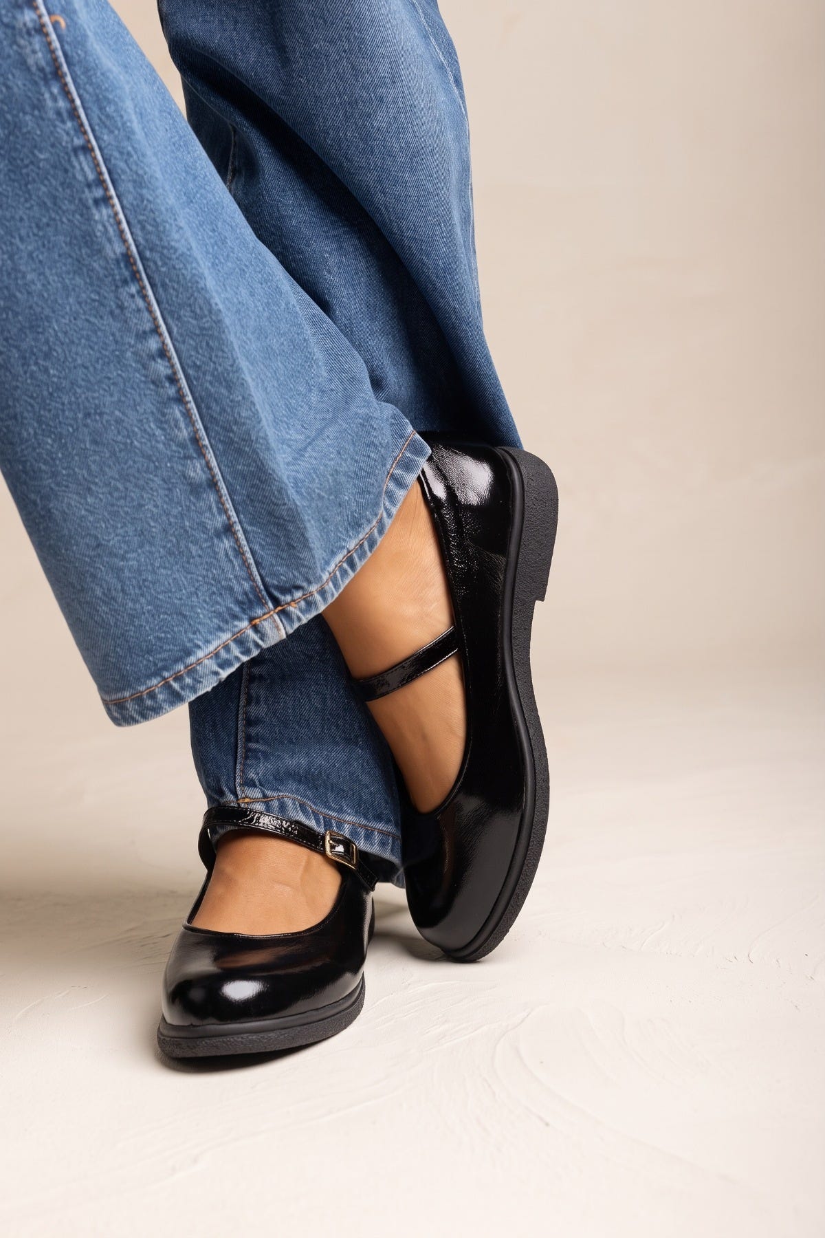Black patent Mary Jane flat with ankle strap and buckle, side view on model in jeans