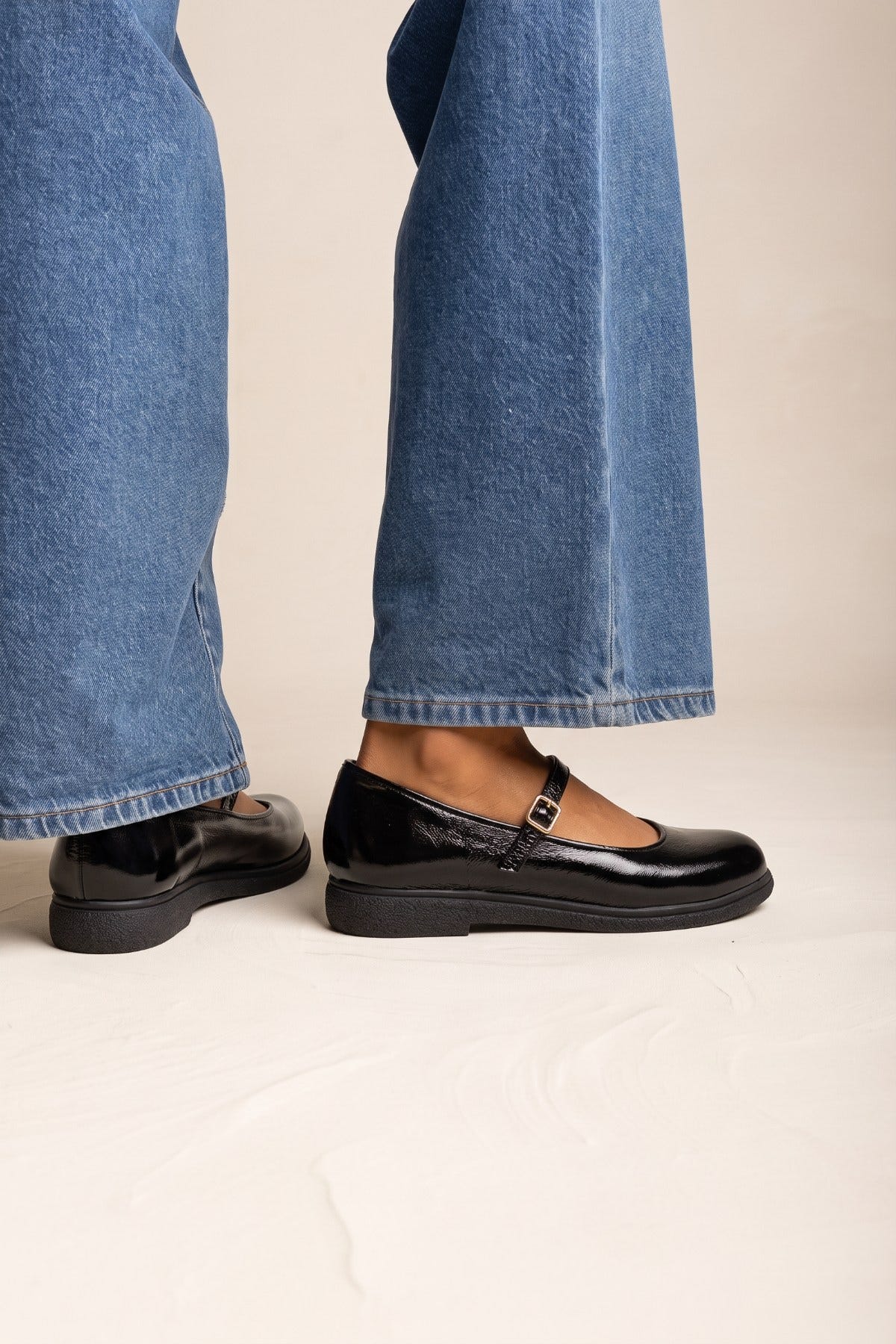 Black patent Mary Jane flat with thick sole and ankle strap, side view worn with jeans