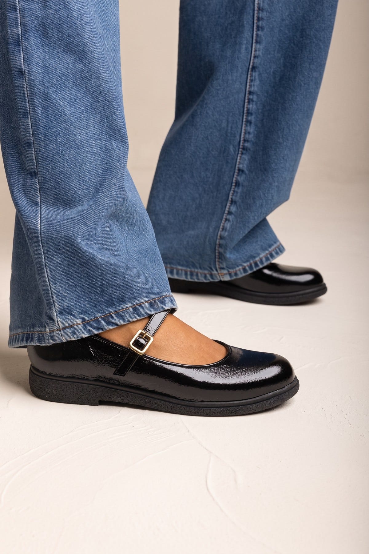 Black patent Mary Jane flat with ankle strap and rounded toe, worn with blue wide-leg jeans
