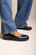 Black patent Mary Jane flat with ankle strap and rounded toe, worn with blue wide-leg jeans