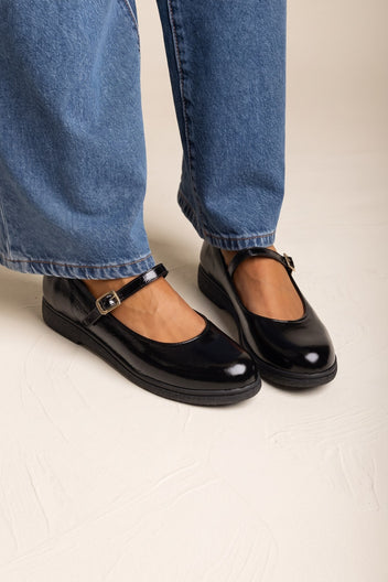 Black patent Mary Jane flats with thick sole and buckle strap, pair worn with blue jeans
