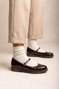 Dark brown patent Mary Jane flats with ankle strap, worn with white socks and beige cuffed trousers
