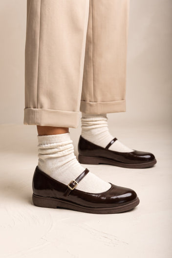 Dark brown patent Mary Jane flats with ankle strap, worn with white socks and beige cuffed trousers