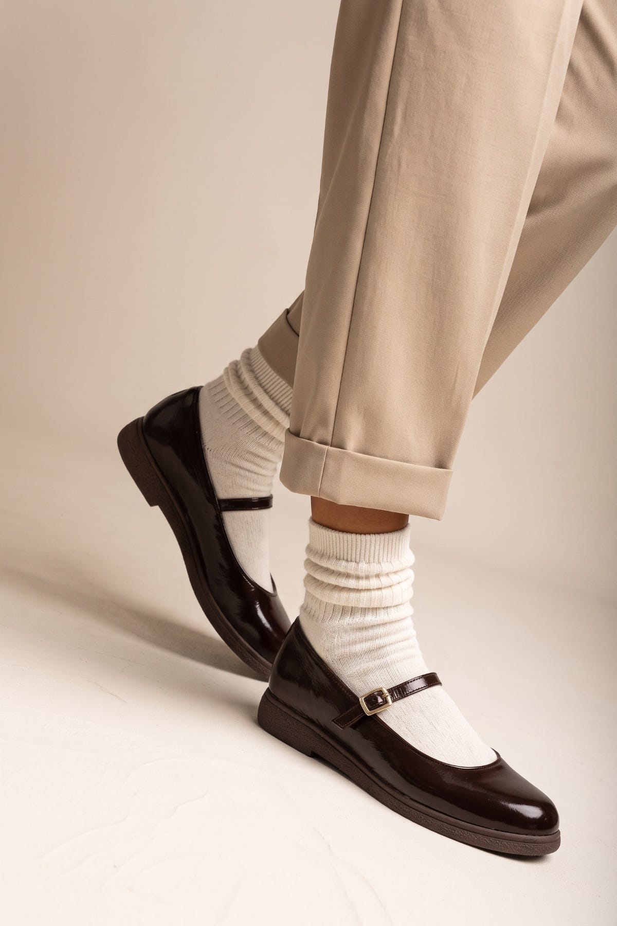Dark brown patent Mary Jane flat with ankle strap and white socks, side view on model legs