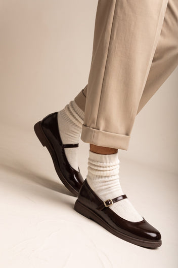 Dark brown patent Mary Jane flat with ankle strap and white socks, side view on model legs