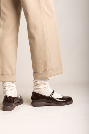 Dark brown patent Mary Jane flats with thick sole, front view of the pair with beige trousers