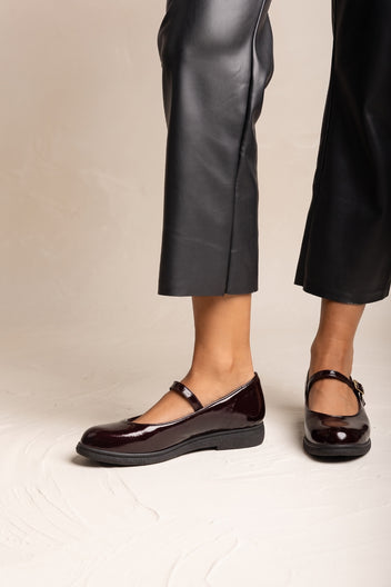 Side view of a pair of bordeaux patent Mary Jane flats with thick sole and ankle strap
