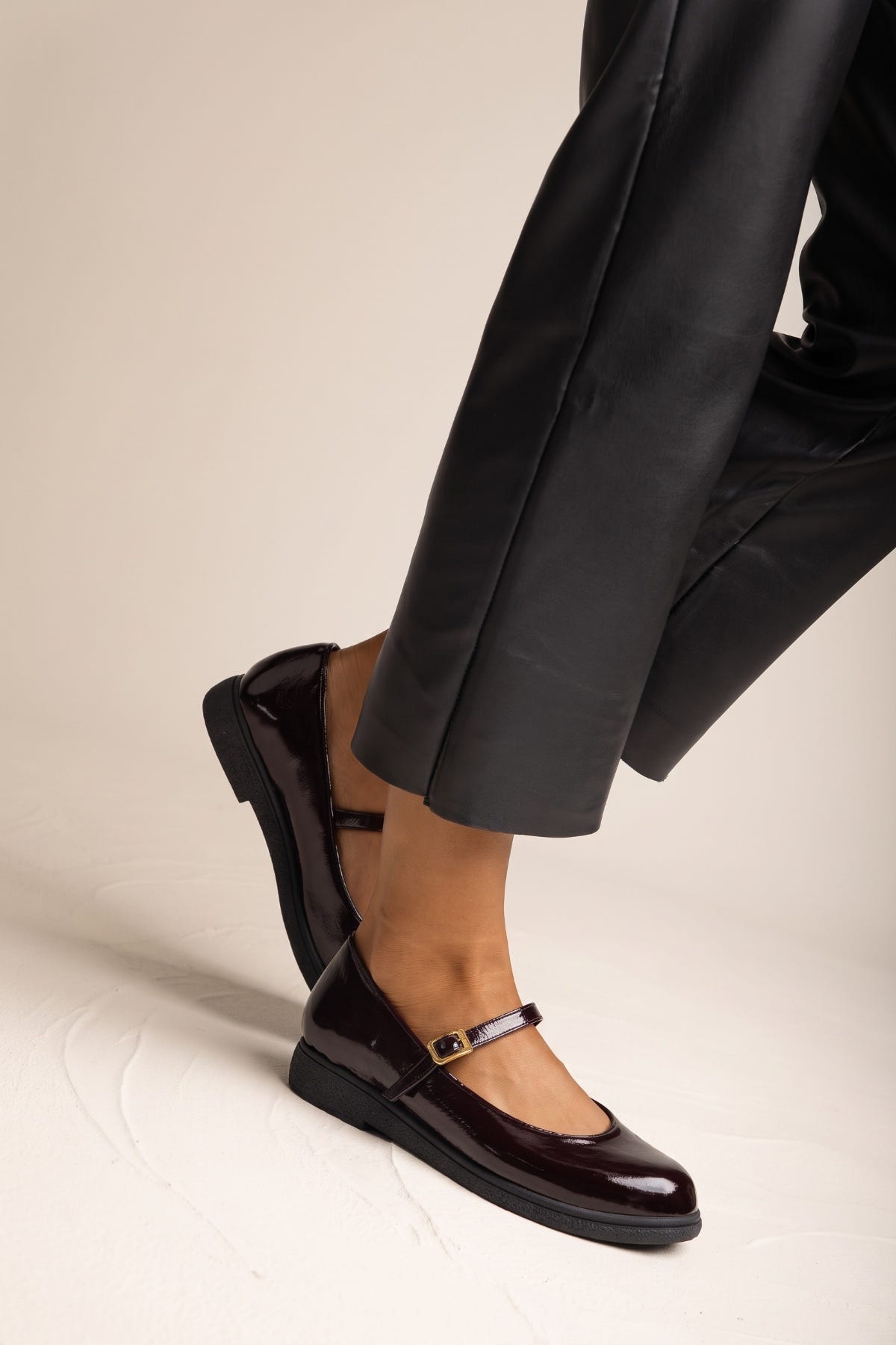 Close side view of bordeaux patent Mary Jane flat with ankle strap and buckle on model