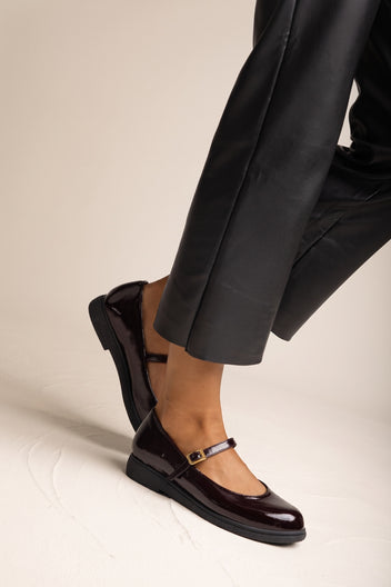 Close side view of bordeaux patent Mary Jane flat with ankle strap and buckle on model