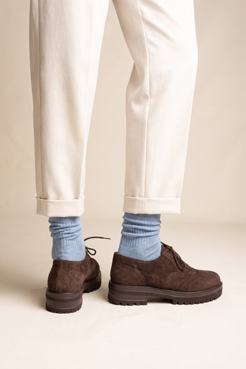 Model wearing brown suede lace up brogue shoes with chunky sole and light blue socks under cream cuffed trousers feet seen from the front