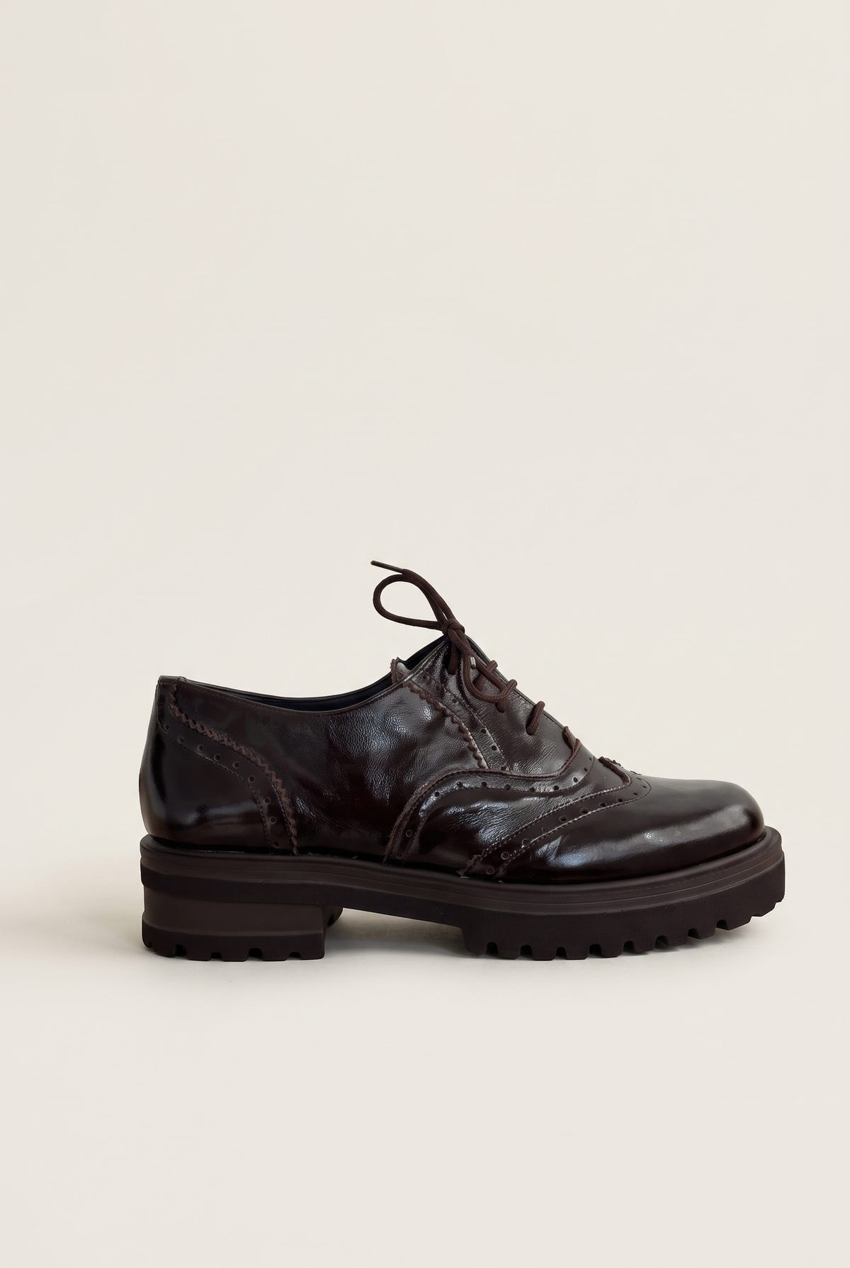 side view of one glossy dark brown patent lace up brogue with perforated wingtip detail and chunky sole