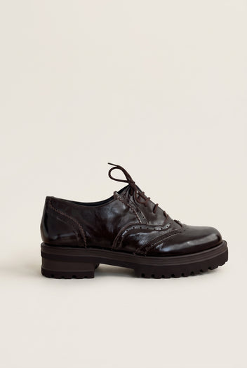 side view of one glossy dark brown patent lace up brogue with perforated wingtip detail and chunky sole