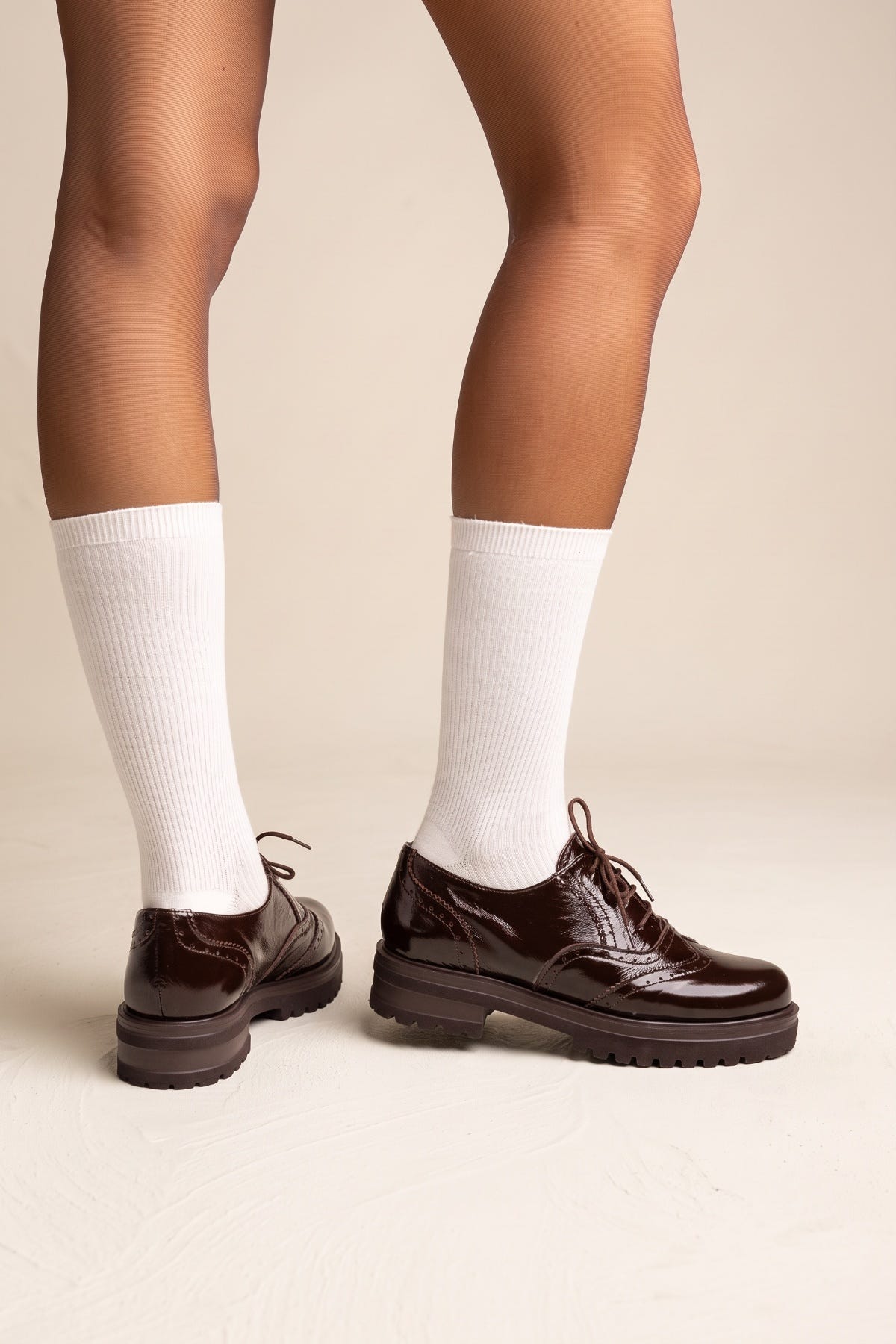 model wearing dark brown lace up brogues with white knee high socks, feet seen from behind