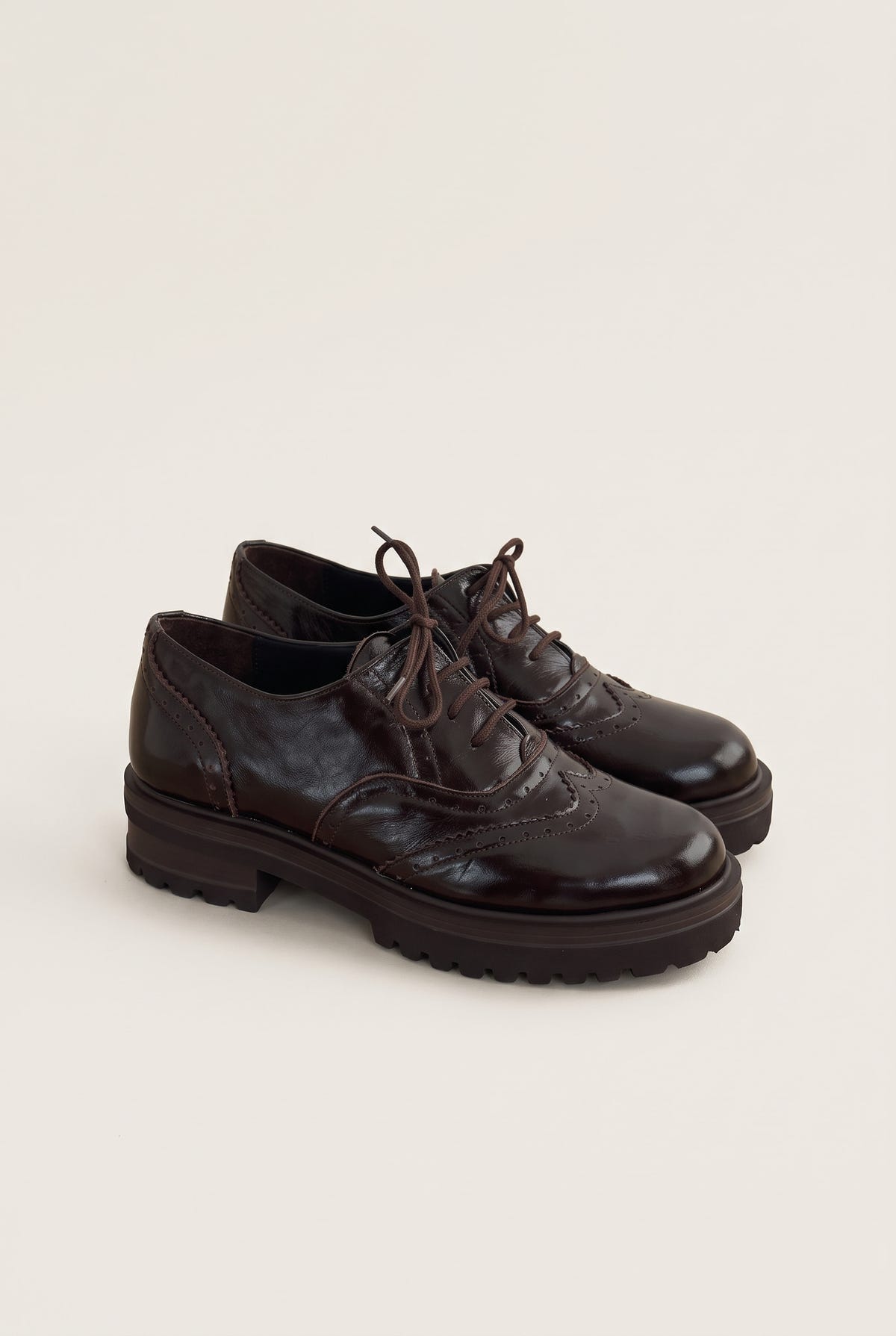 pair of glossy dark brown lace up brogues angled to show the chunky lug sole and brown laces