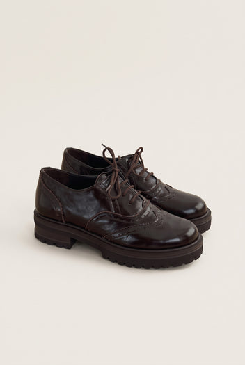 pair of glossy dark brown lace up brogues angled to show the chunky lug sole and brown laces