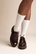 model wearing glossy dark brown patent lace up brogues with chunky soles and white ribbed socks