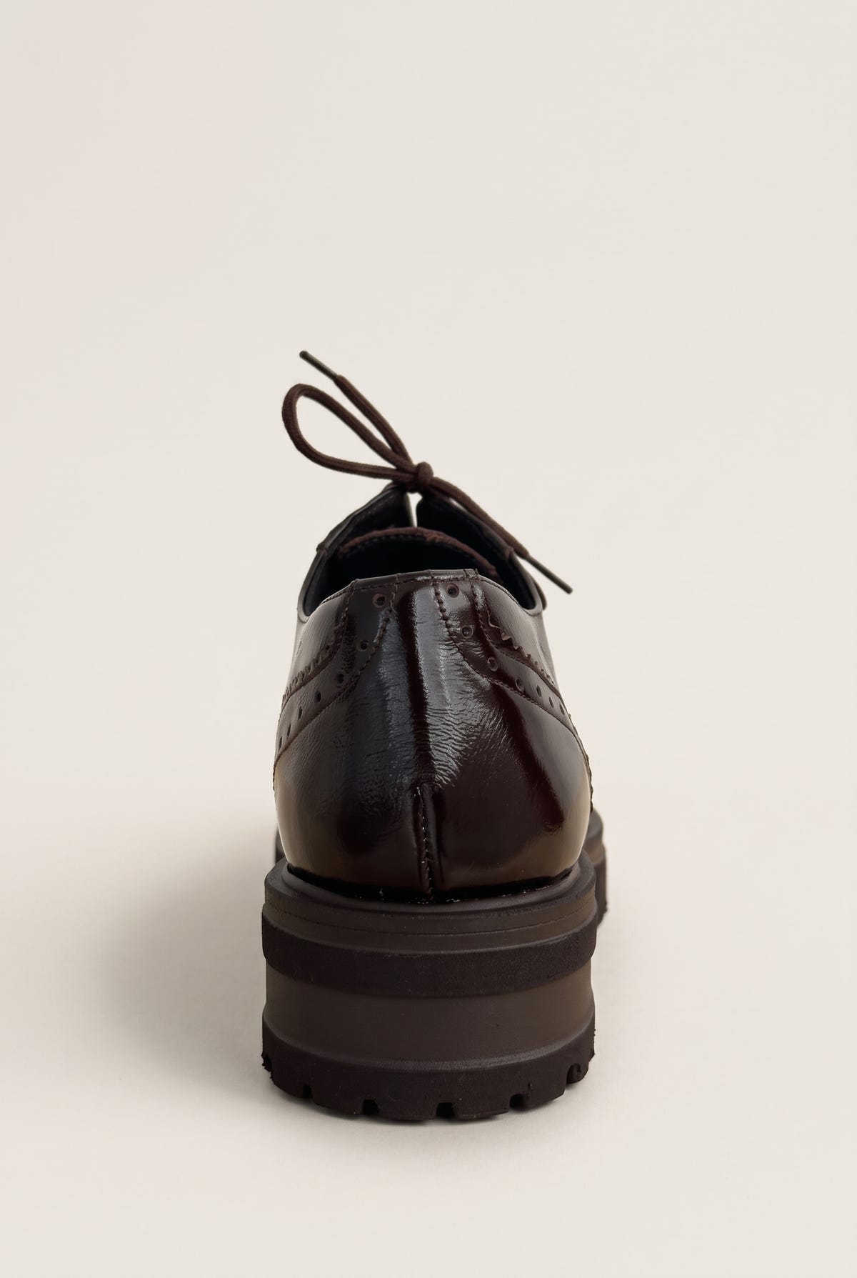 back view of one glossy dark brown lace up brogue showing the heel tab and a thick lug sole