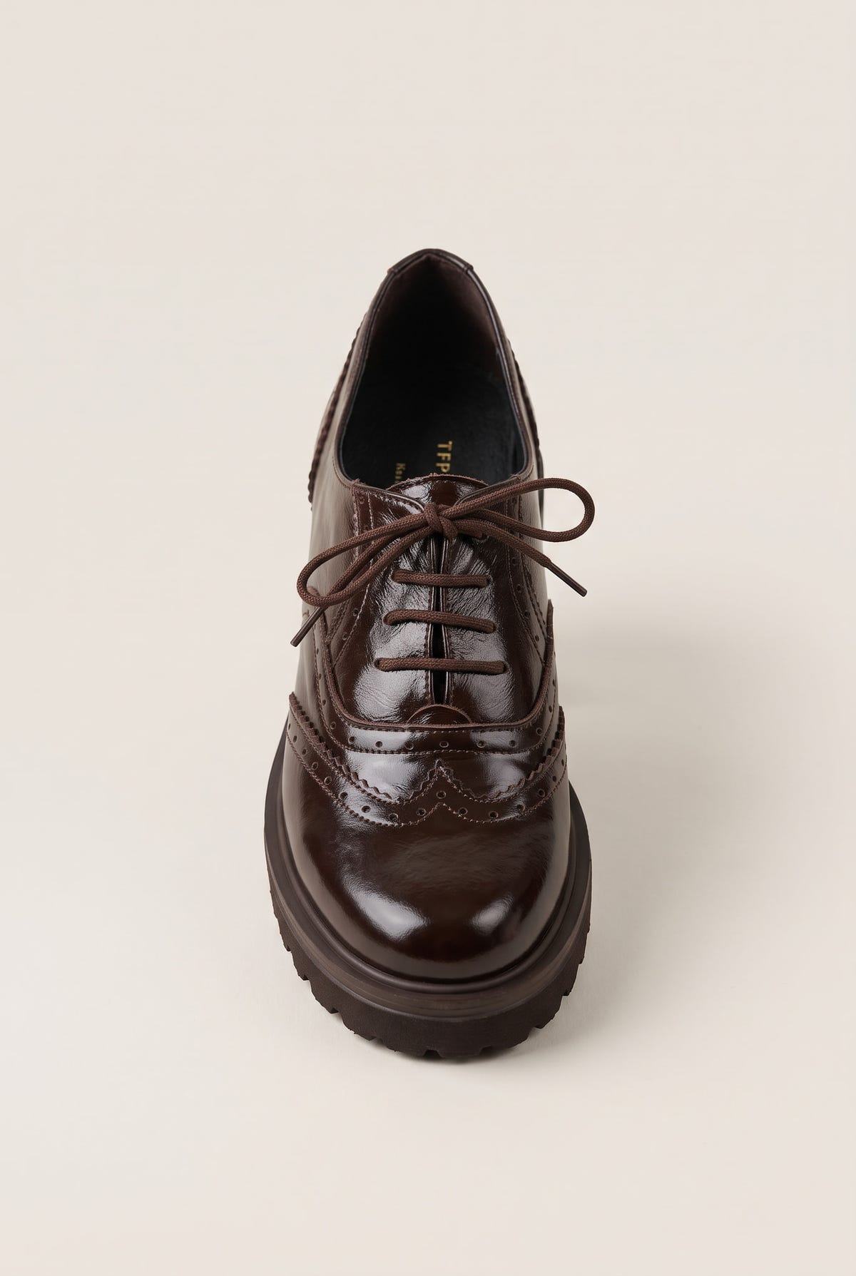 front view of a glossy dark brown lace up brogue with brown laces and a thick ridged lug sole