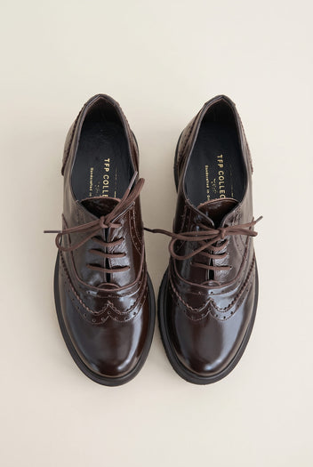 top view of a pair of glossy dark brown patent lace up brogues with brown laces and perforated toe detail