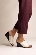 Model wearing beige and black wedge heel mules with square toes and burgundy trousers