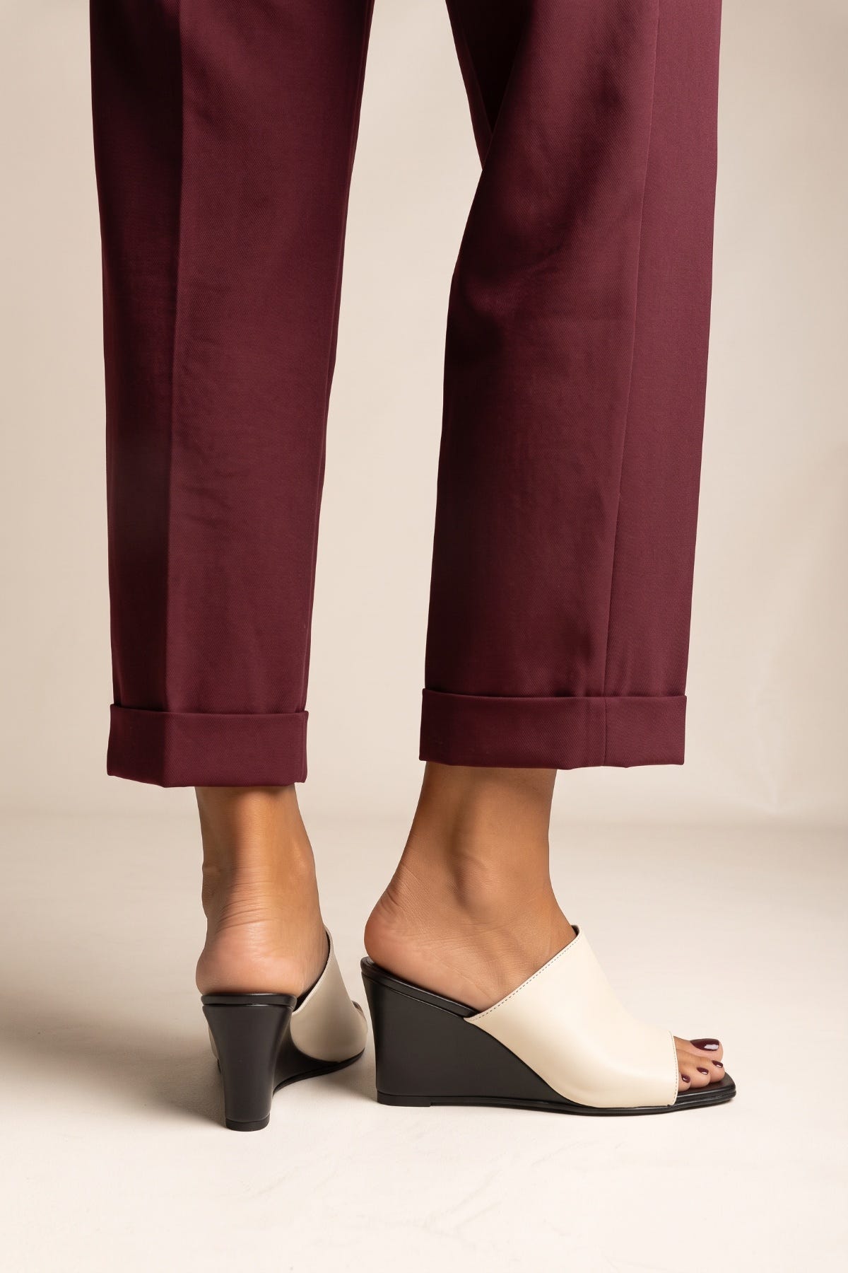 Front view of model in beige and black wedge mules with square toes and burgundy cuffed trousers