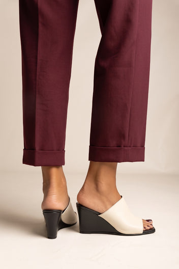 Front view of model in beige and black wedge mules with square toes and burgundy cuffed trousers