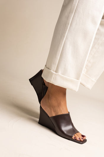 Model in brown matte square toe wedge mules seen from a side angle with cream cuffed trousers