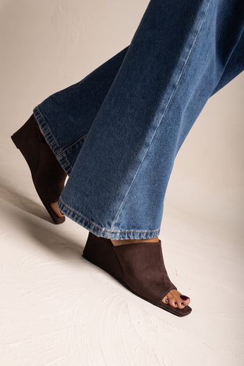 Close-up of brown suede square toe wedge mule on model foot beneath blue denim jeans