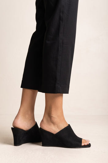 Side view on model of black suede wedge mule with open square toe, wide upper band and a solid wedge heel