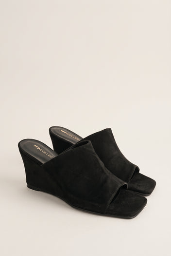 Three-quarter view of a pair of black suede wedge mules with square open toes and wide vamp bands