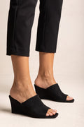 Front view on model of black suede wedge mules with wide diagonal strap, open square toe and high wedge heel