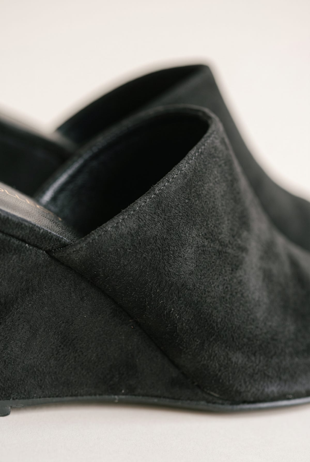 Close-up of black suede wedge mule showing the soft wrap-over vamp, stitching and wedge side