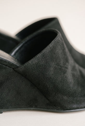 Close-up of black suede wedge mule showing the soft wrap-over vamp, stitching and wedge side