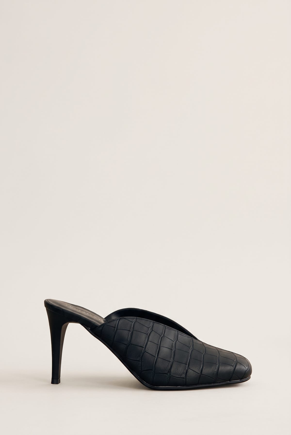 Side view of a black croc-embossed mule with a squared toe, a low vamp and a slim stiletto heel