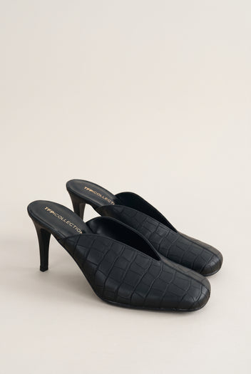 Angled view of a pair of black croc-embossed leather mules with squared toes and slim stiletto heels