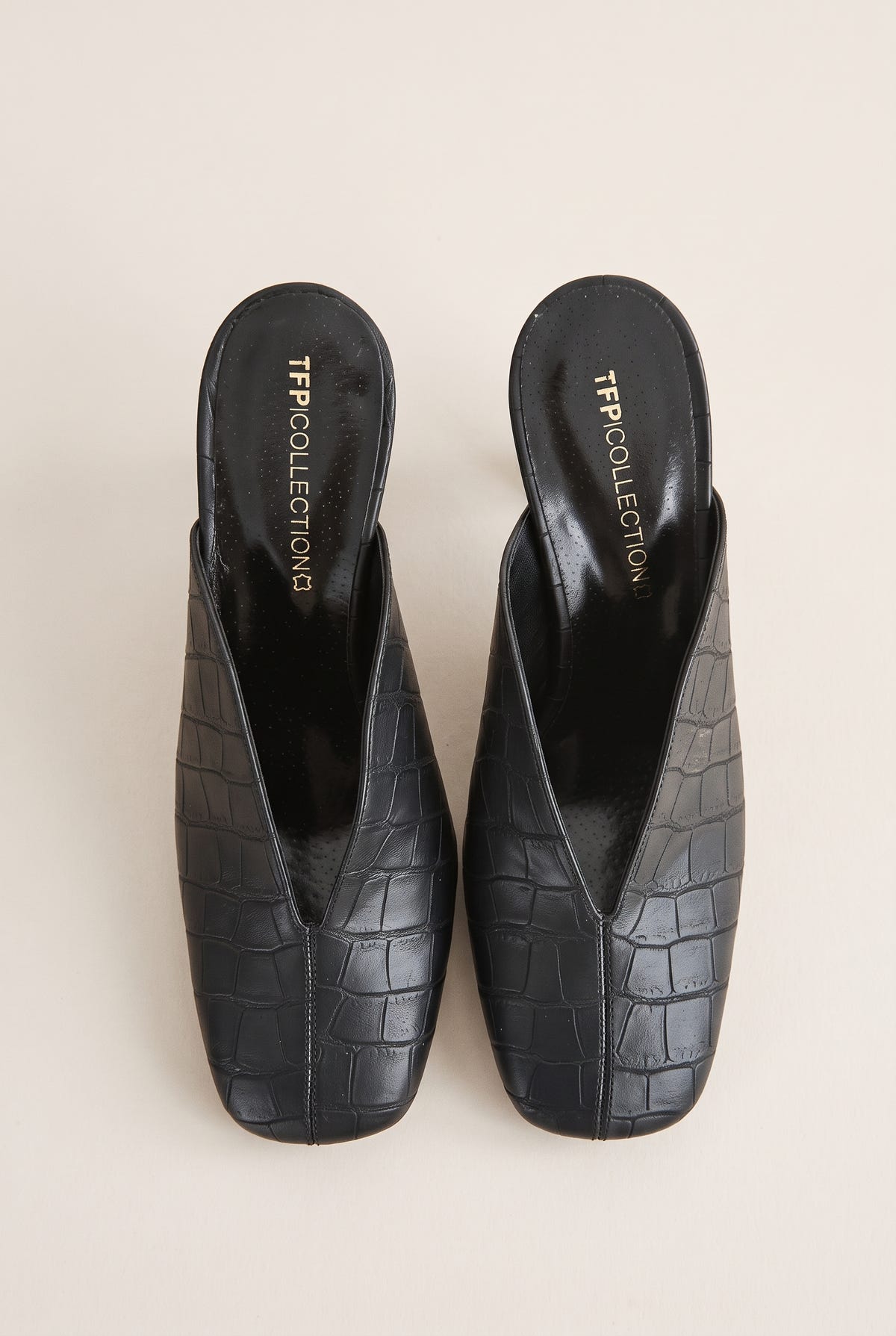 Top view of a pair of black croc-embossed leather mules with squared toes and deep V openings at the vamp