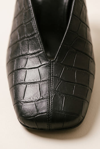 Close-up of a black croc-embossed mule toe showing the squared shape and the deep V opening at the vamp