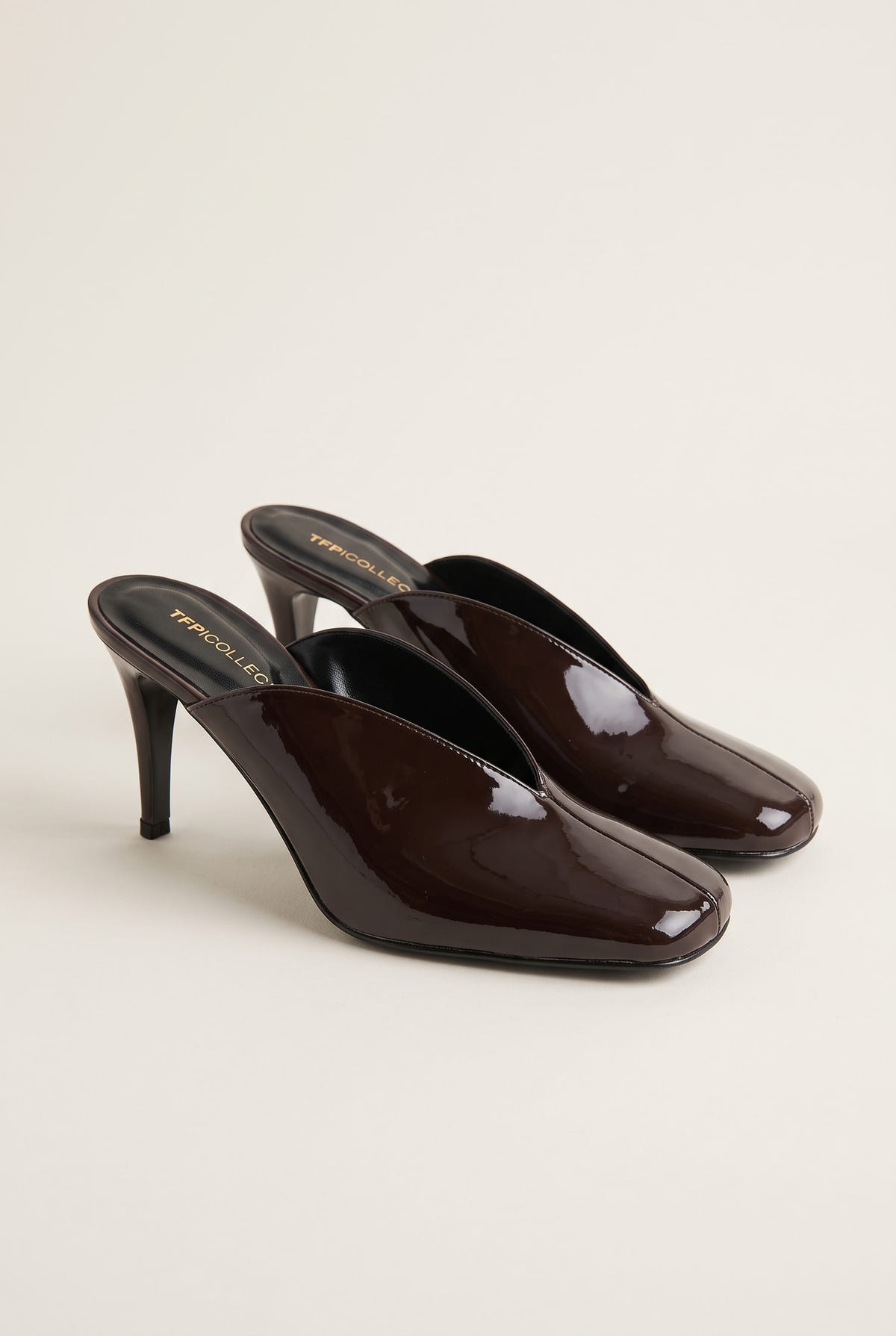 pair of glossy dark brown patent stiletto mules angled to show the square toe and slim heel