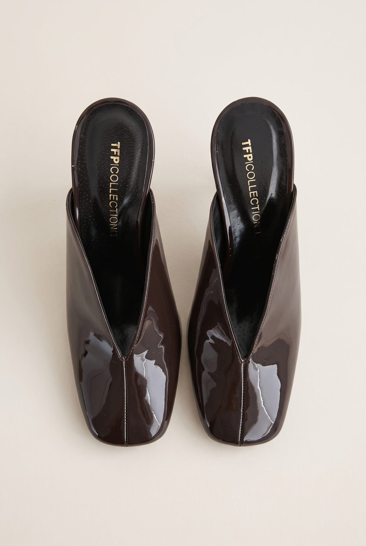 top view of a pair of glossy dark brown patent square toe mules with a deep V cut vamp