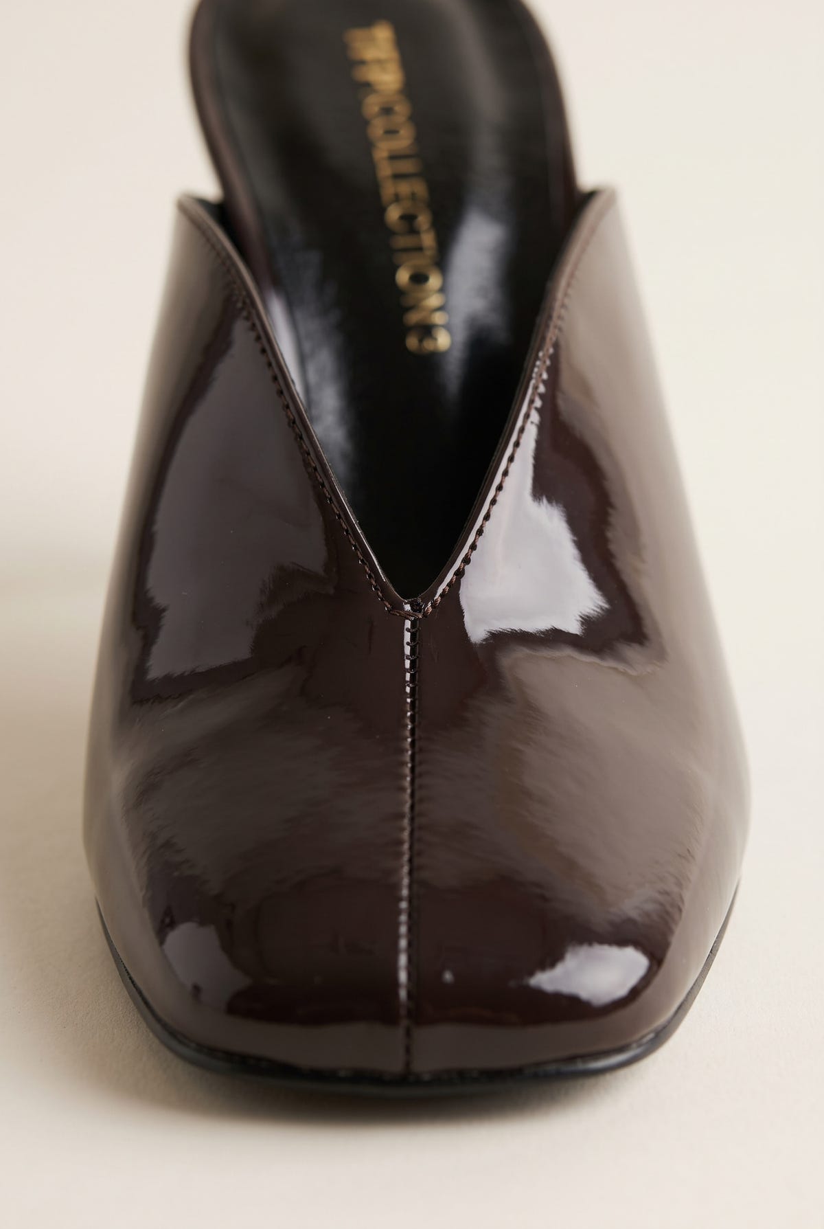 close-up of the glossy dark brown patent square toe and V shaped vamp seam on a stiletto mule