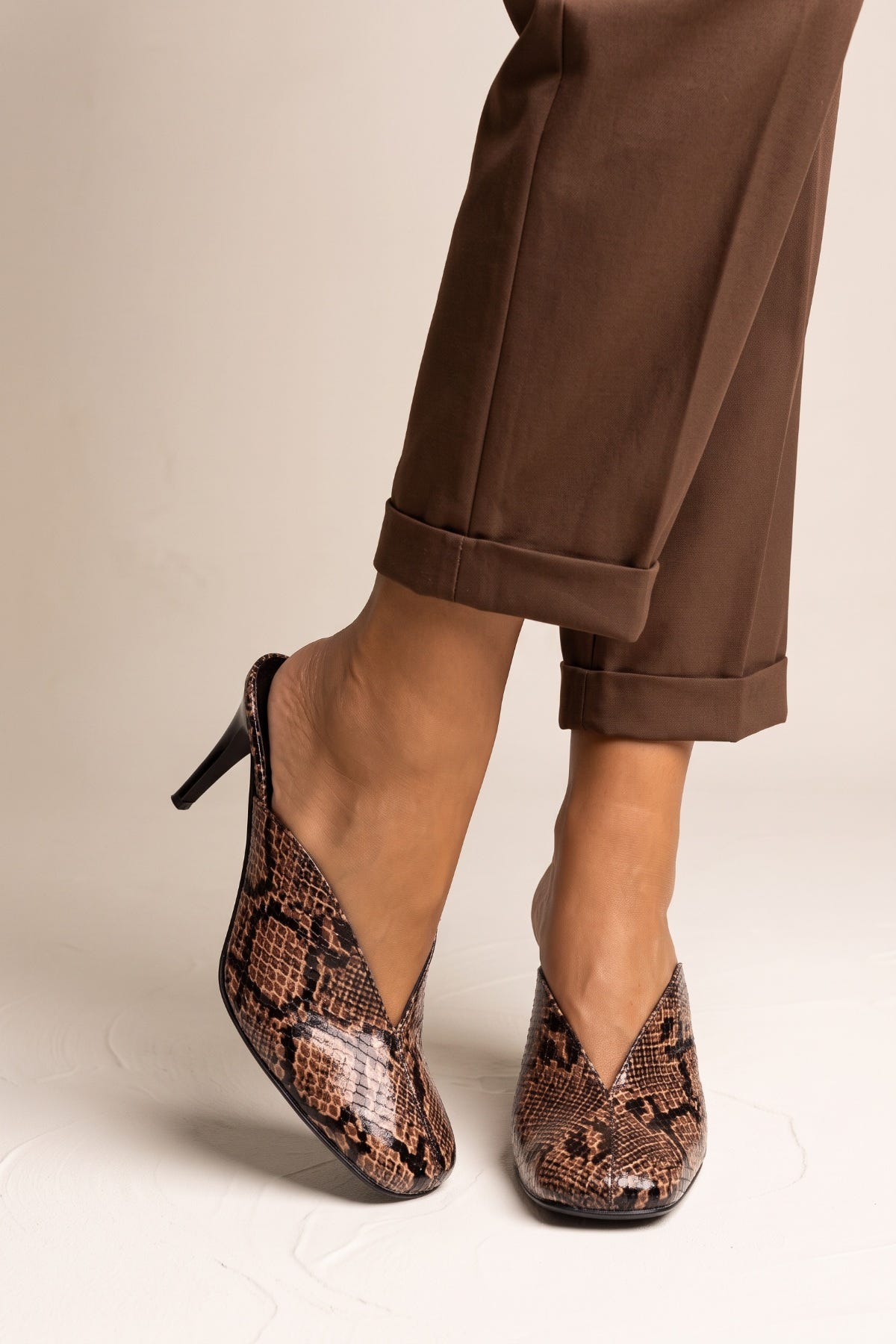 model wearing brown snake print stiletto mules with cuffed brown trousers, feet angled forward