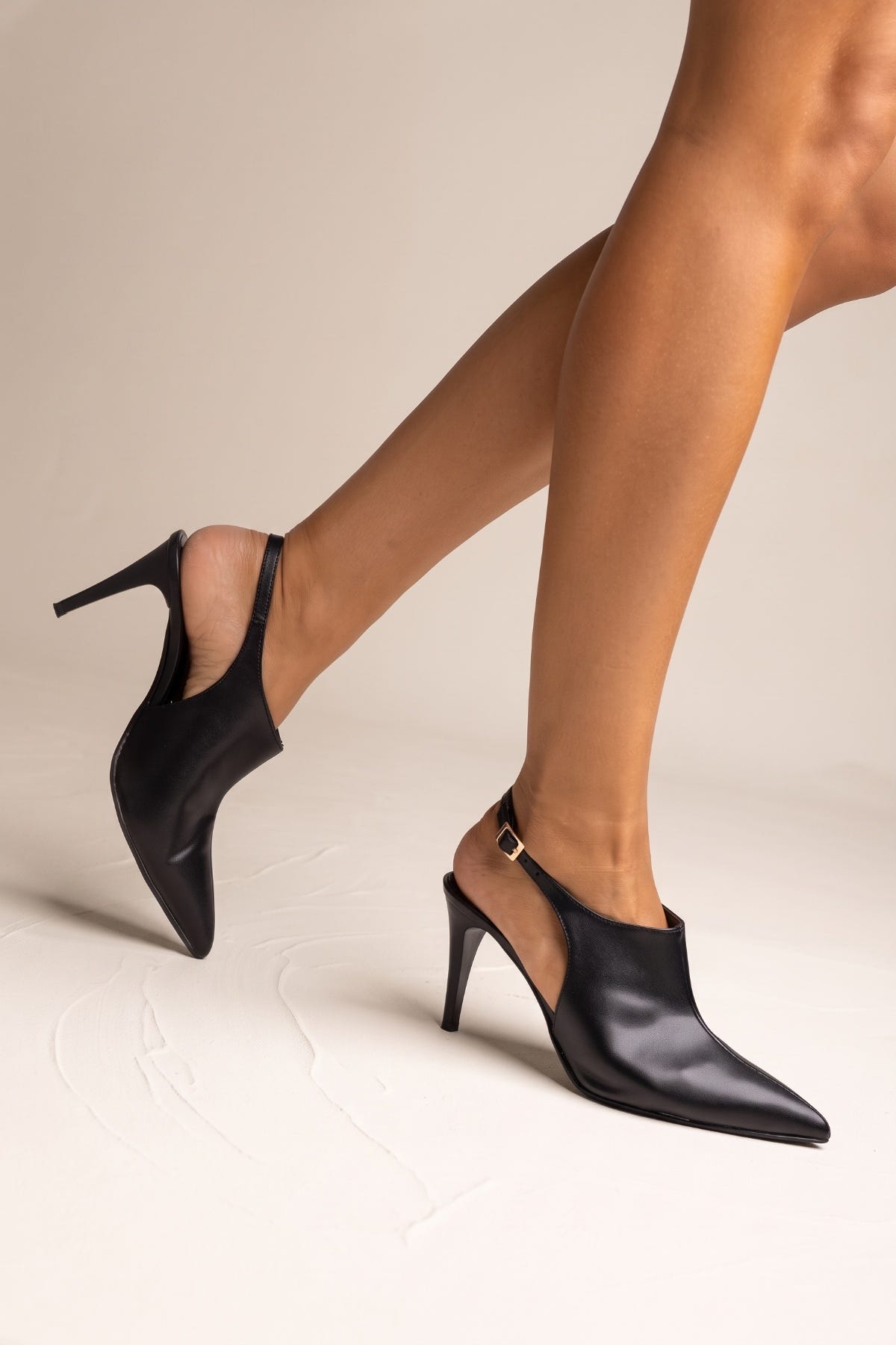 Model wearing black matte pointed toe stiletto slingback pumps with a thin heel, leg raised in side view