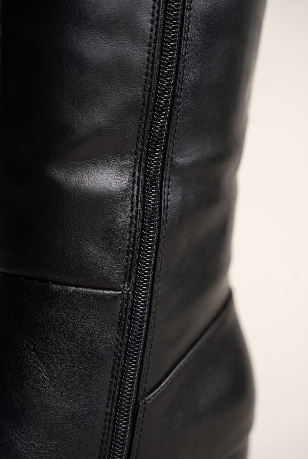 Close-up of a black leather knee-high boot side zip with stitched seams and panelled lower shaft