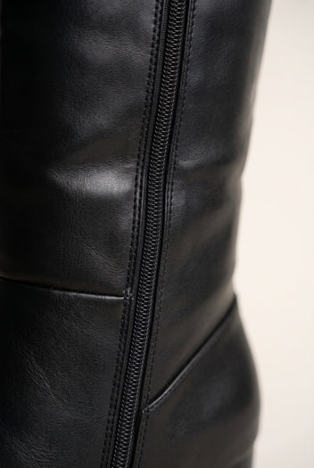 Close-up of a black leather knee-high boot side zip with stitched seams and panelled lower shaft