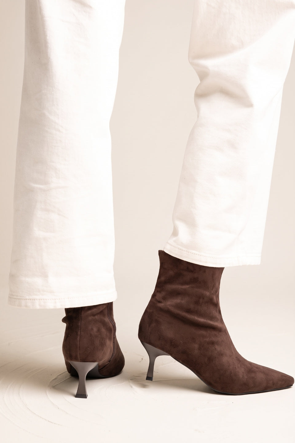 Model in white trousers wearing brown suede pointed toe ankle boots with slim kitten heels