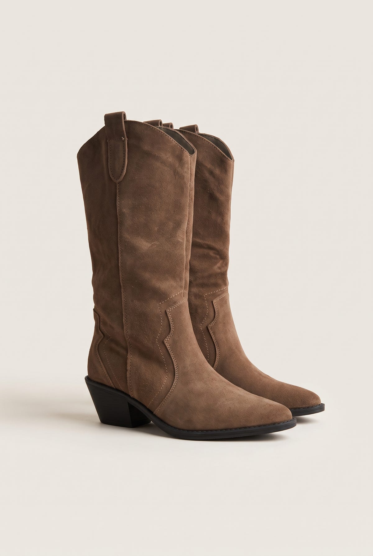 Pair of taupe suede knee-high cowboy boots with block heels and pointed toes, angled front view