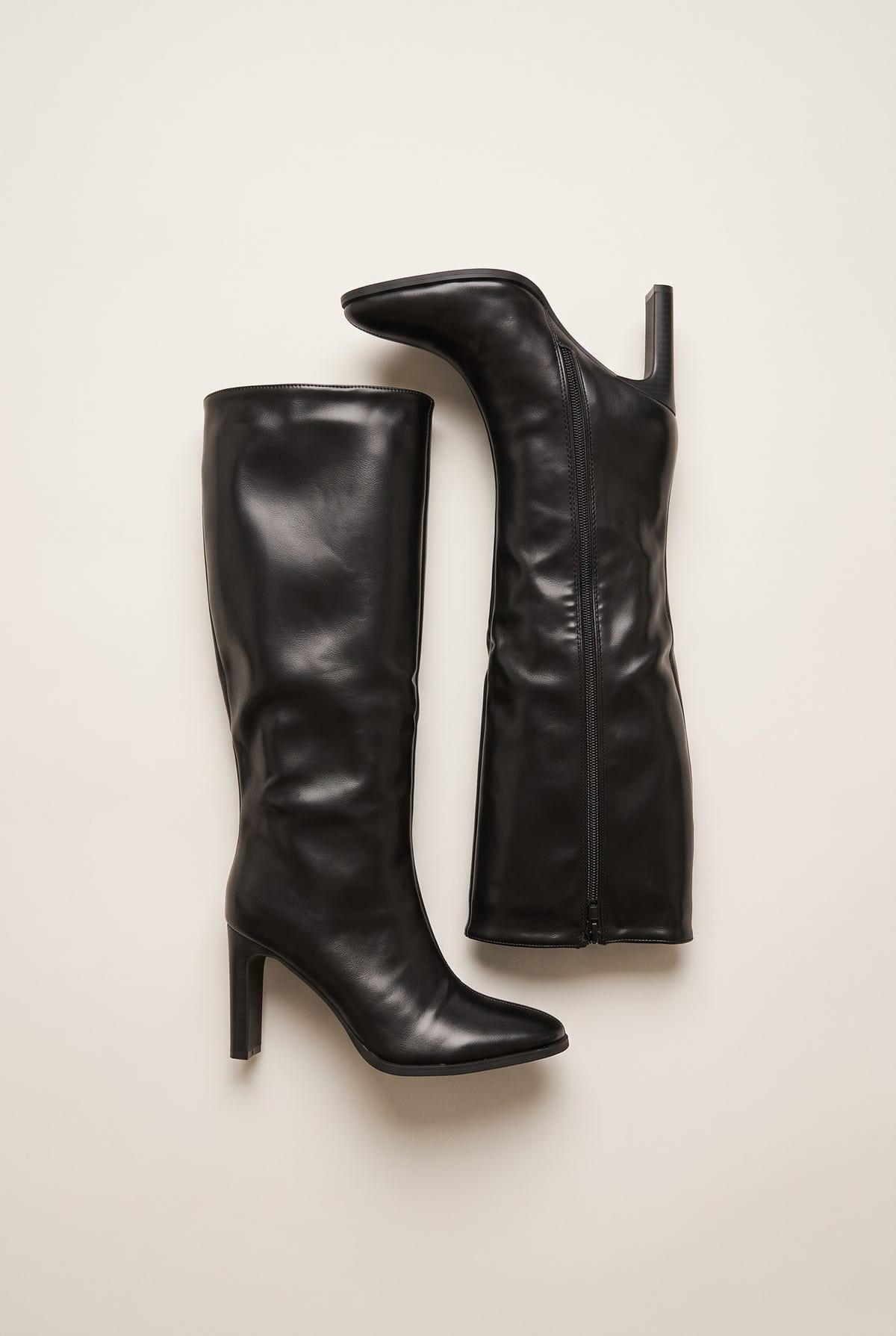 Top view of black leather-look knee-high boots lying on their sides showing long shafts pointed toes and a zip along the inner edge
