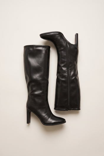 Top view of black leather-look knee-high boots lying on their sides showing long shafts pointed toes and a zip along the inner edge